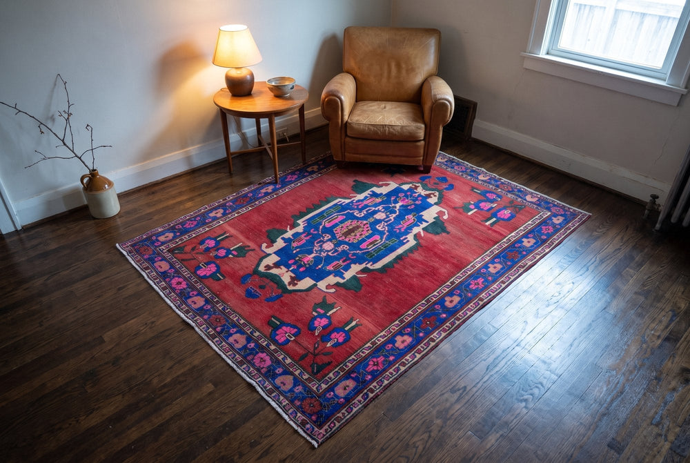 A red Sirjan rug with a large blue medallion in front of a tan leather armchair and a lamp table, seen from high in the room