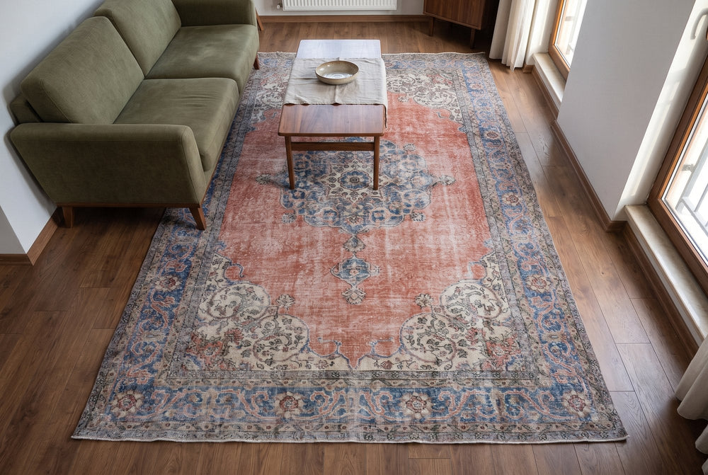 A faded terracotta Isparta rug with a blue medallion and cream corners under a walnut table and an olive sofa, seen from above