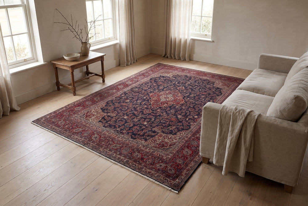 A navy Hamedan rug with a rust medallion and burgundy border in a bright living room with a linen sofa and an oak side table