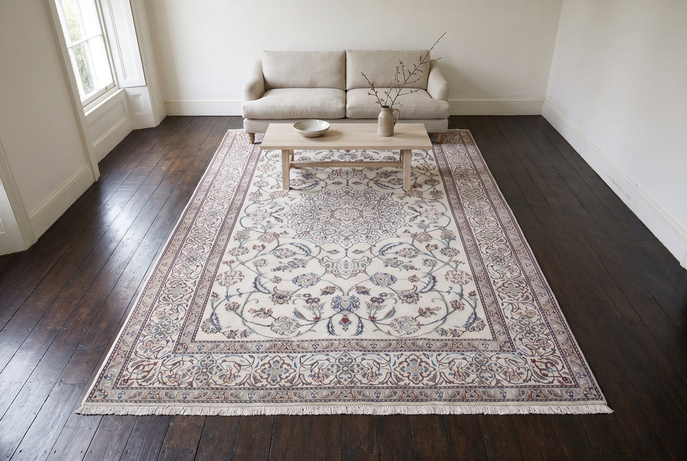 A cream Nain rug with a blue-gray medallion on dark oak boards under a pale wood coffee table and a linen sofa, seen from high in the room