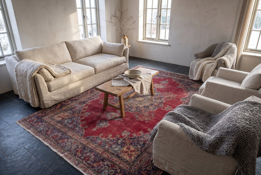 A red vintage Tabriz rug with a navy medallion and border on a dark slate floor in a winter living room with a linen sofa, armchairs and chunky knitted throws