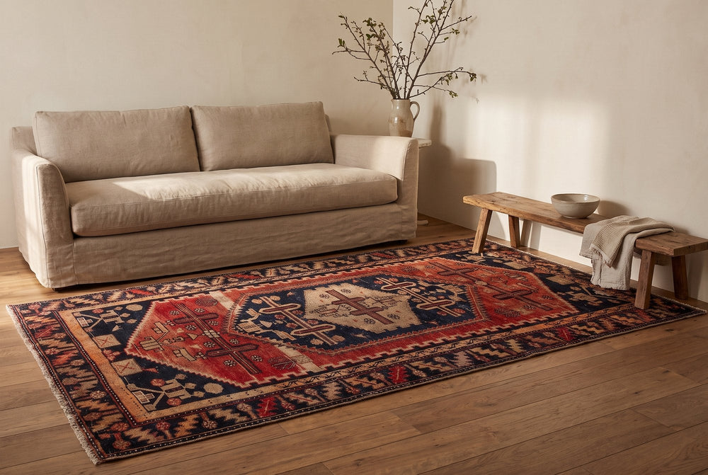 A rust and navy vintage Lori rug with a nested cream medallion and cross motifs on an oak floor in front of a linen sofa and a wooden bench