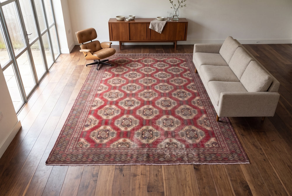 A faded red Torkaman rug with ivory guls in a mid-century living room with a walnut sideboard, a leather lounge chair and a low sofa