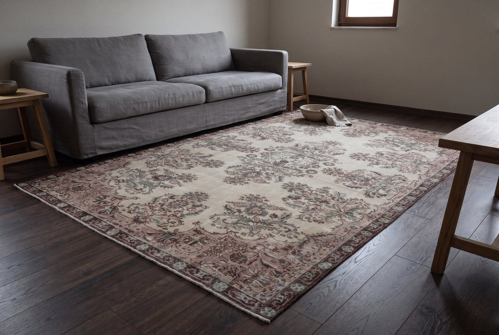 A pale cream vintage Isparta rug with faded rose and green flower sprays and a dusty rose border brightening a dark oak floor in front of a gray linen sofa