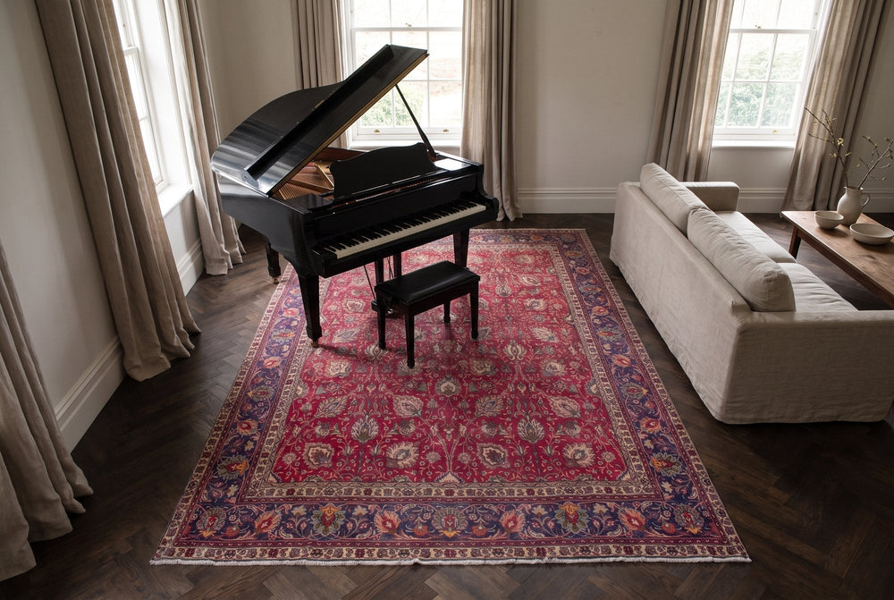A red vintage Tabriz rug with an all-over palmette design and a navy border under a black grand piano and its bench, on a dark herringbone floor