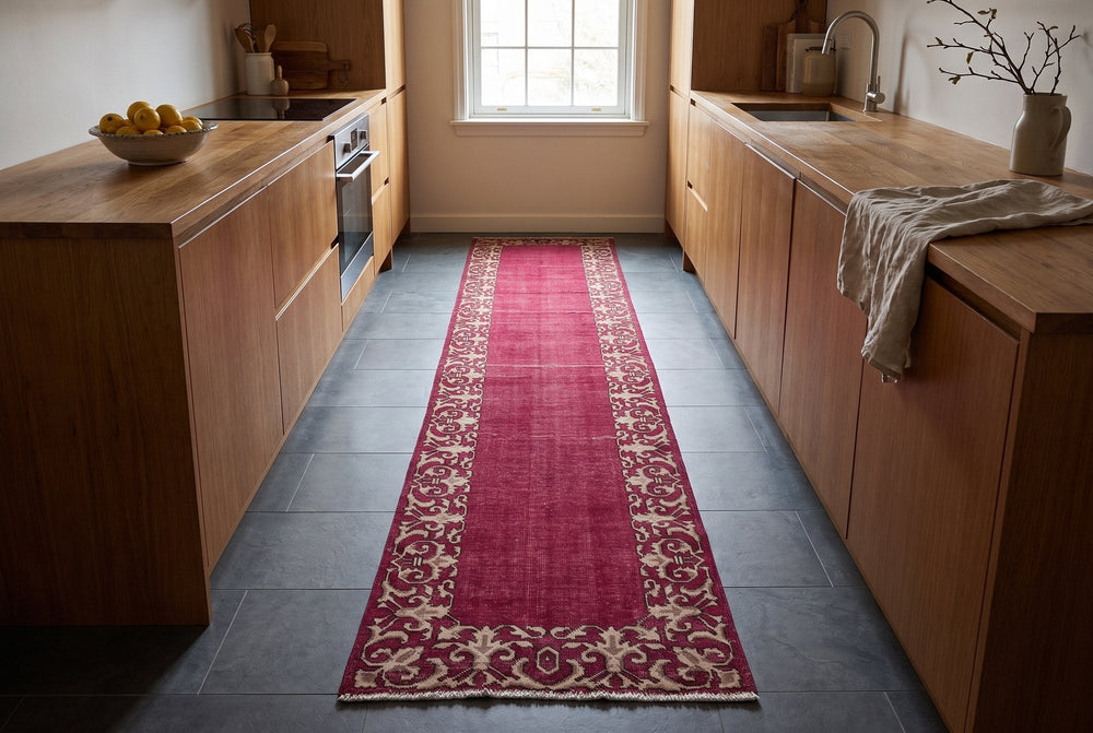 A long raspberry red vintage Tabriz runner with a wide ivory arabesque border lying flat along a galley kitchen on gray porcelain tiles