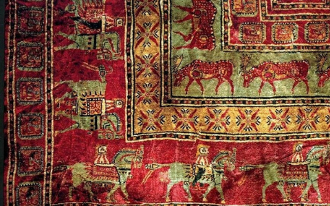 A corner of the Pazyryk carpet showing rows of horsemen and grazing deer on a red field