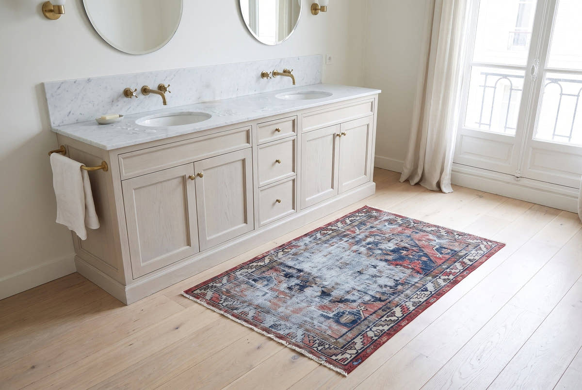 A faded blue and red vintage Persian Saveh rug beside a marble double vanity in a Paris bathroom