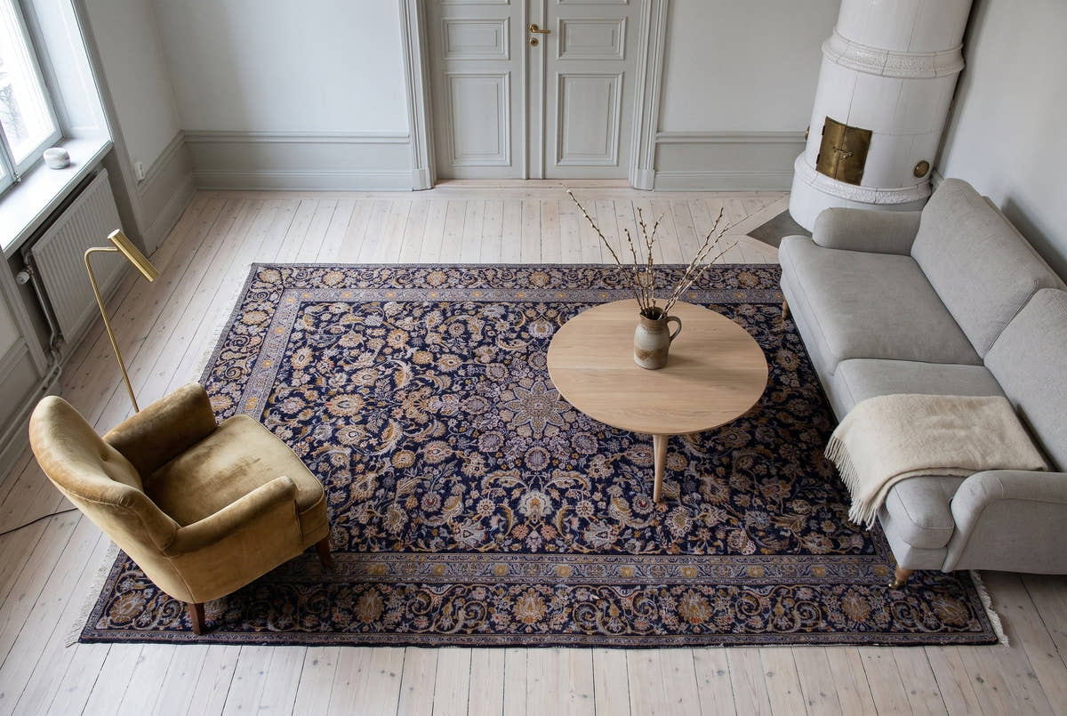 A navy and gold vintage Persian Kashan rug seen from above in a bright Stockholm apartment living room with a white tiled stove