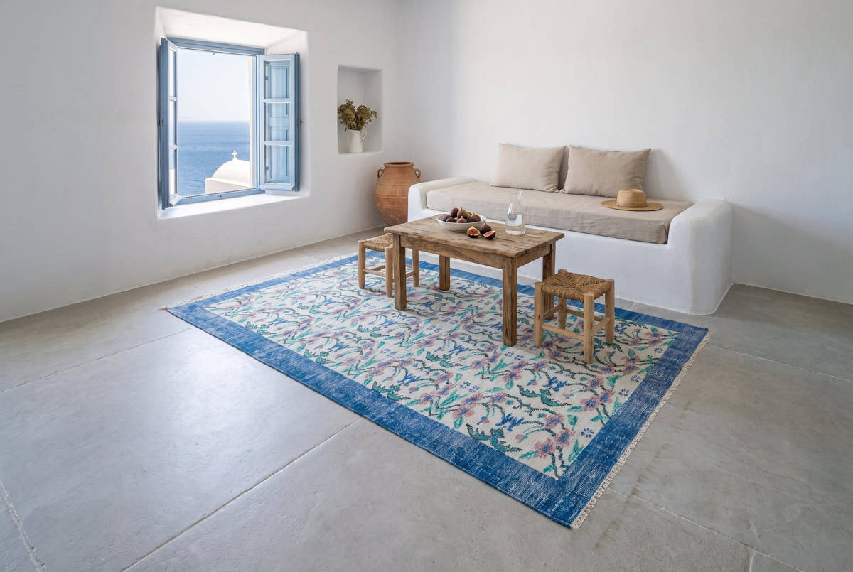 A cream and denim blue vintage Turkish Manisa rug in the living room of a whitewashed Cycladic house on the island of Paros, Greece, midday