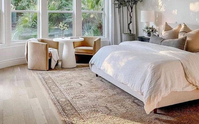 Faded vintage rug beside a bed in a sunlit bedroom