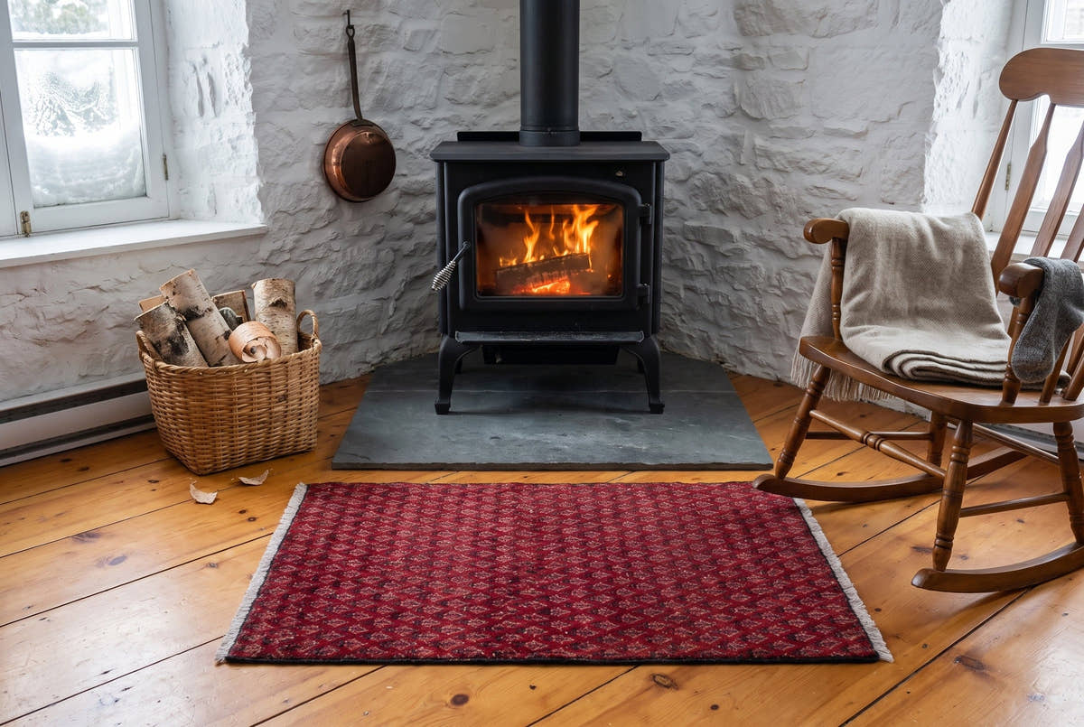 A red vintage Persian rug covered in small botteh motifs by a wood stove in an old stone house in Quebec City