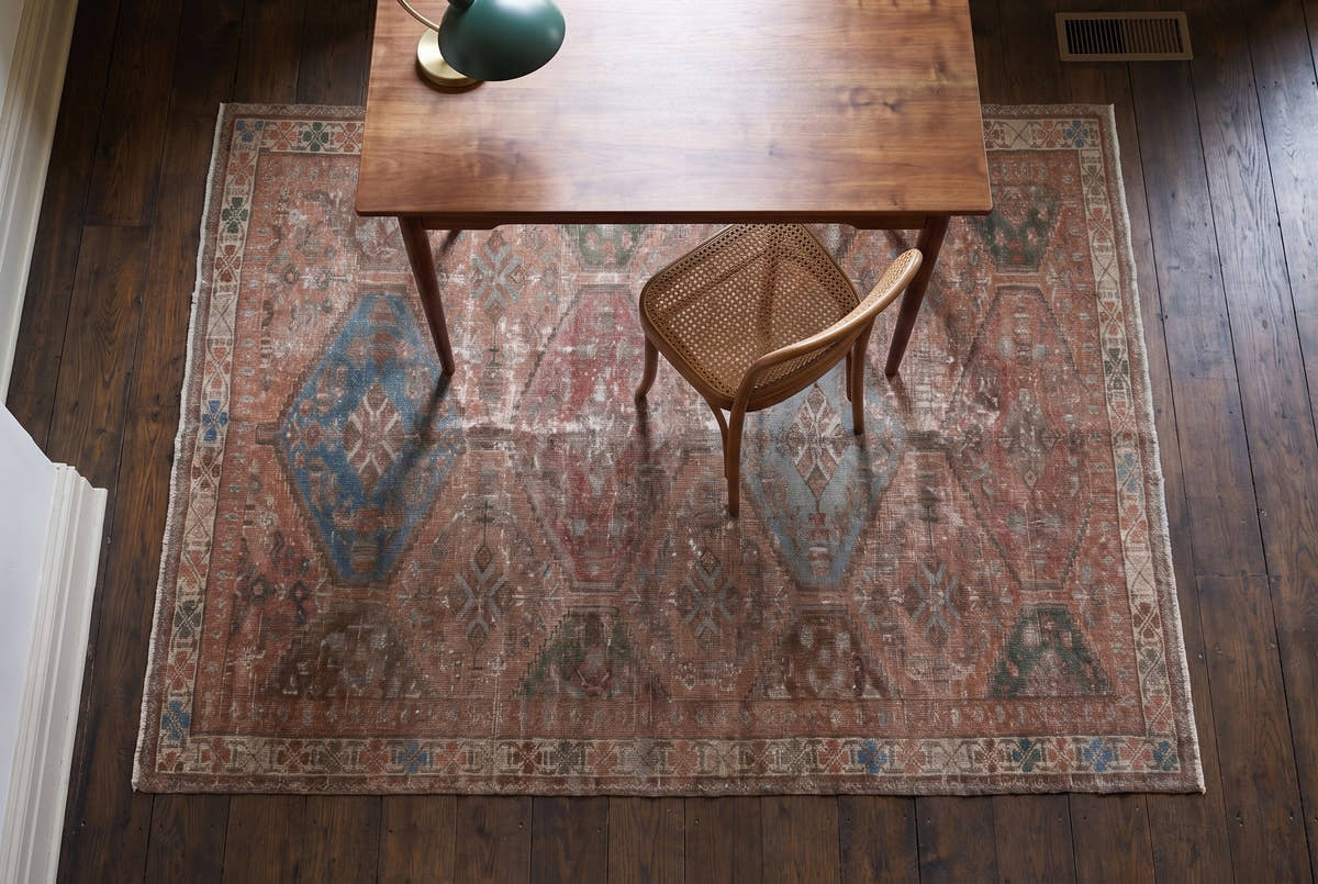 A faded rose vintage Persian Shiraz rug seen from above under a walnut desk and cane chair in a Brooklyn brownstone study