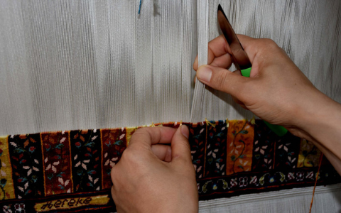 Hands knotting a fine rug on an upright loom, the woven part visible below