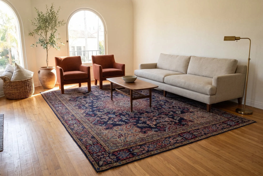 Sunny living room with arched windows, a navy Kerman rug under the front legs of an oatmeal sofa, two terracotta armchairs and a walnut table