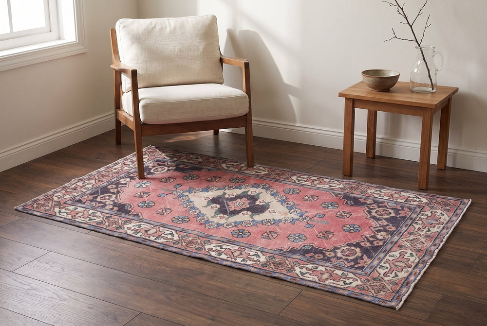 A rose vintage Isparta rug with a stepped cream medallion, navy corners and an ivory border under a wooden armchair on dark walnut boards
