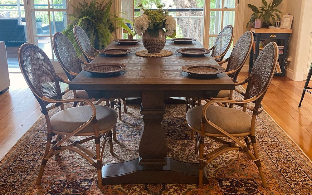 A long wooden dining table with six rattan armchairs, every chair standing on a large vintage rug