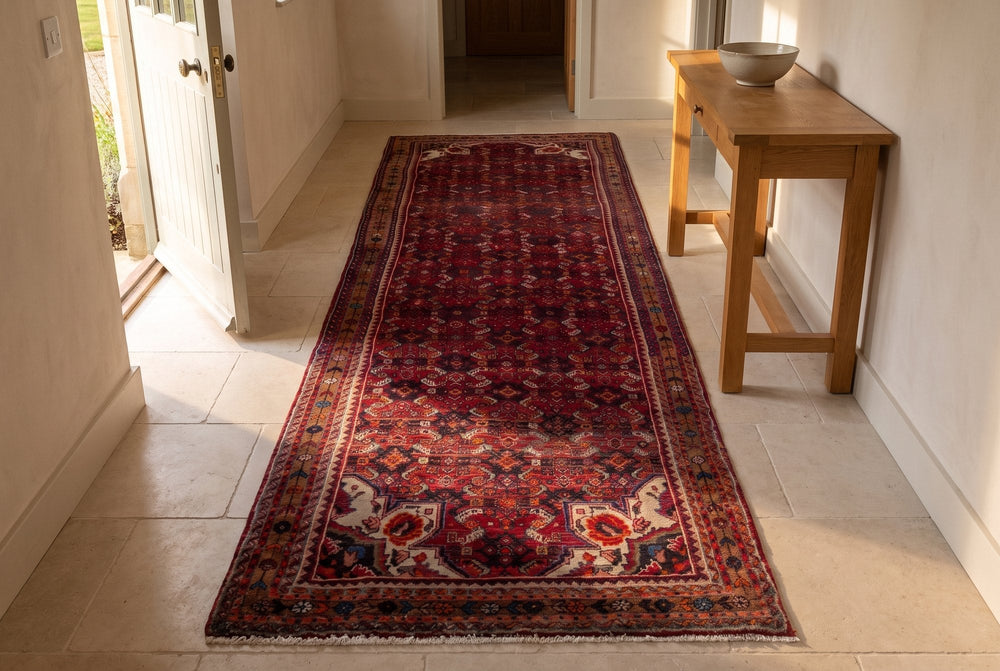 A wide red Hosseinabad runner with ivory corner motifs lying on pale limestone in an entry hall, beside an oak console and an open front door