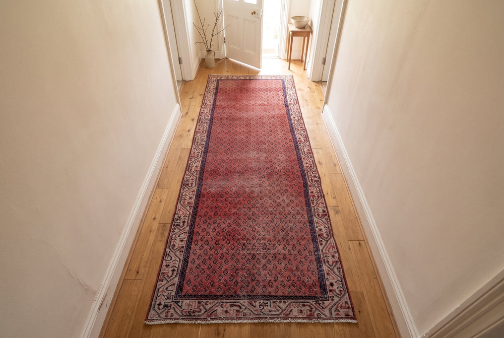 A faded red Arak runner lying flat down an oak hallway, seen from high above at one end
