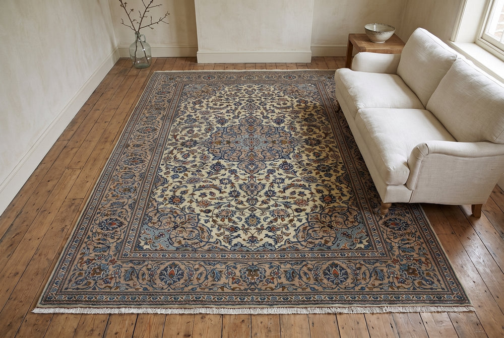 An ivory Kashan rug with a blue-gray medallion and wide taupe border under a linen sofa on old pine boards, seen from high at one end