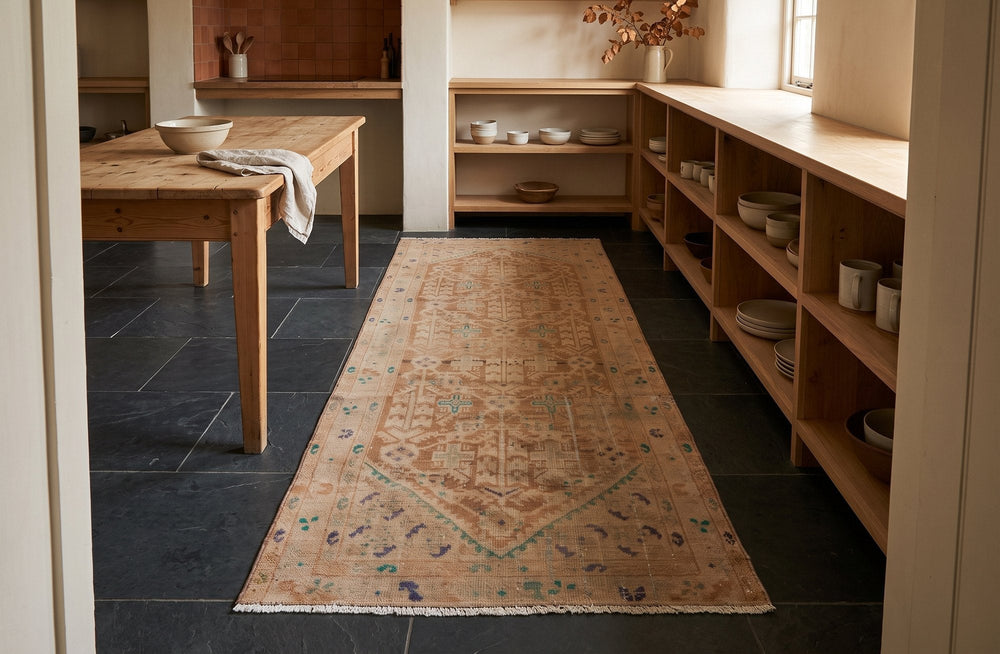 A faded tan Malayer runner with a long six-sided medallion on dark slate tiles in a farmhouse kitchen with pine shelves