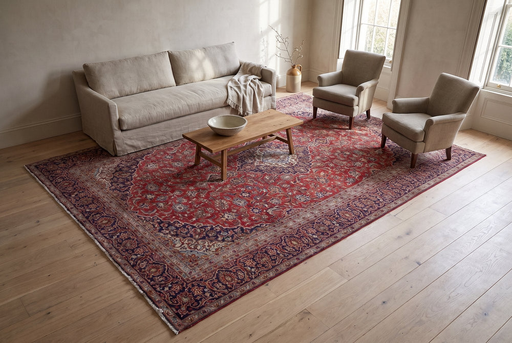 An oversized red vintage Kashan rug with a navy medallion and floral border under a linen sofa, two armchairs and an oak coffee table in a bright living room