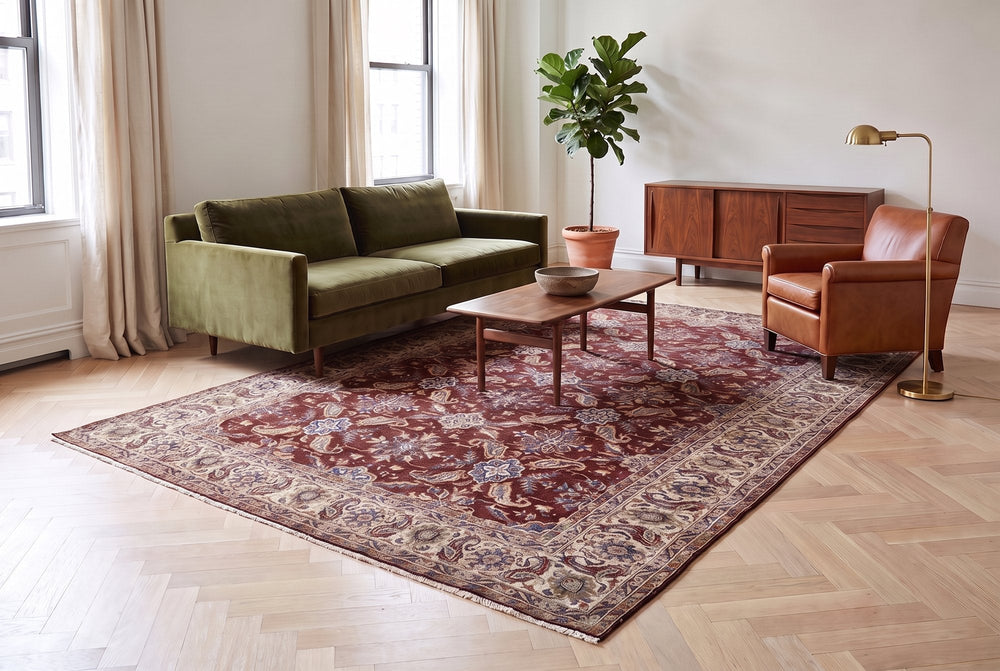 Sitting room on pale herringbone oak with a worn oxblood Persian rug with a cream border under a walnut coffee table, olive velvet sofa behind