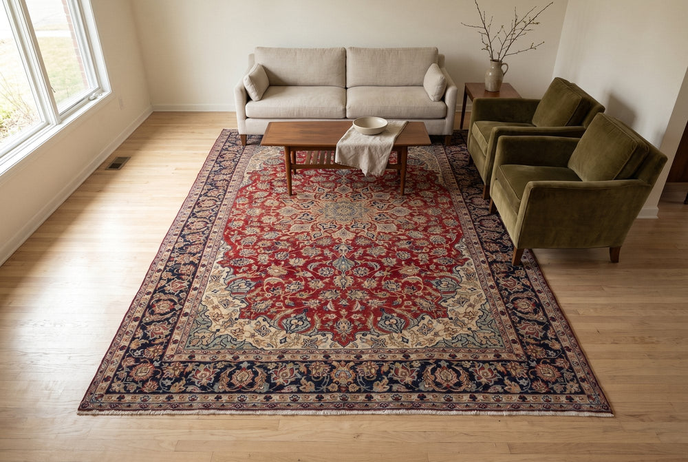 A deep red Najafabad rug with a cream-cornered medallion and navy border under a walnut coffee table, a linen sofa and olive velvet armchairs