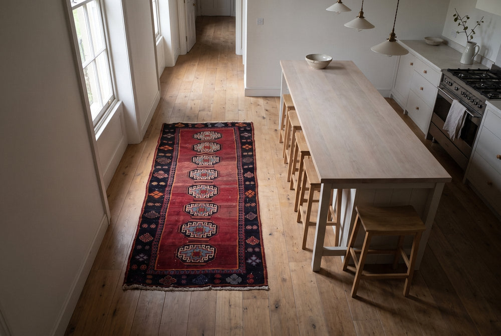 A red Saveh runner with a column of octagonal medallions on oak boards beside a pale wood kitchen island, seen from high above