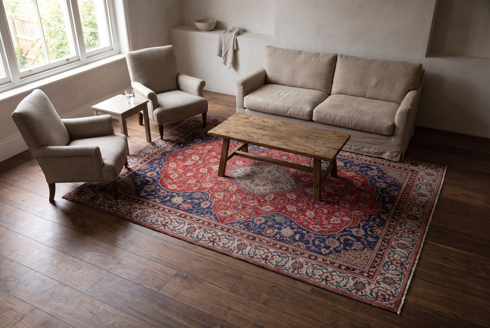 A red and navy Mahal rug holding a linen sofa, two armchairs and a wooden coffee table in a bright living room, seen from a high corner
