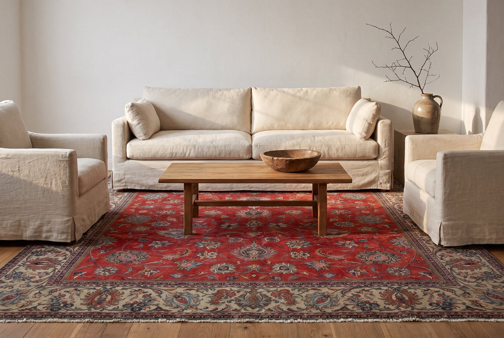 A deep red Sarouk rug with scattered flower sprays and a wide beige border under a linen sofa, two linen armchairs and an oak coffee table in a white plaster living room