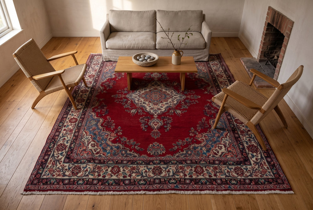 A deep red vintage Hamedan rug with an ivory medallion centered on a sofa, two rope armchairs and an oak coffee table, with a brick fireplace off to one side