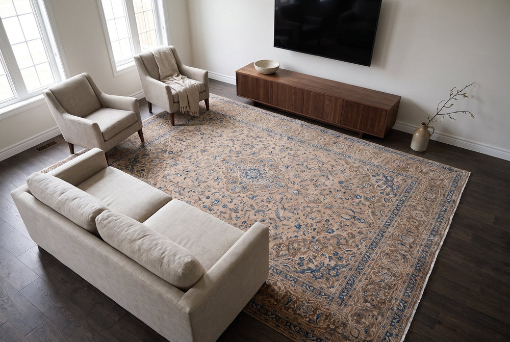 A beige vintage Kashan rug with soft blue drawing holding a sofa and two armchairs, stopping short of a walnut media console under a wall-mounted TV