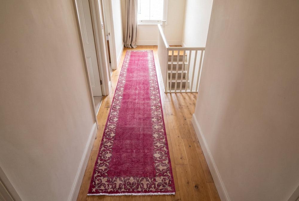 A long raspberry Tabriz runner with a cream scrolling border down an upstairs landing, the staircase at the far end
