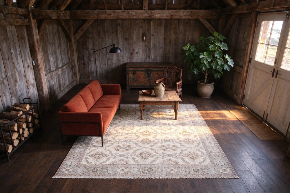 A long ivory Turkish rug in a converted barn with weathered board walls, a rust wool sofa, an old wooden chest and a fig tree.