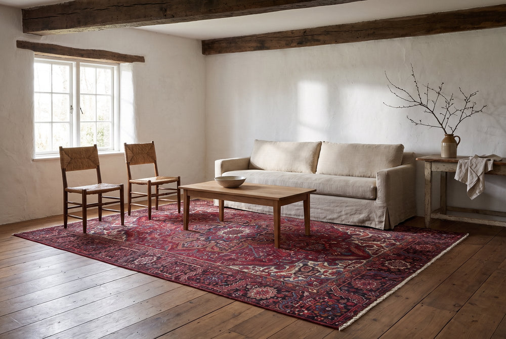 A red vintage Heriz rug with a bold geometric medallion and ivory corners in a farmhouse living room with beams, a linen slipcovered sofa and rush-seat chairs