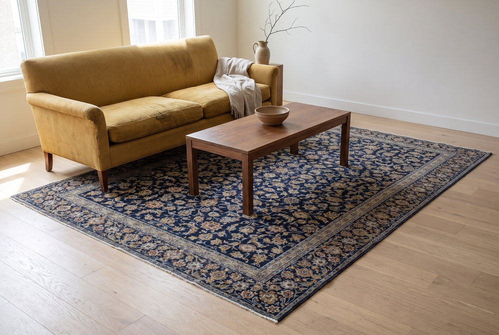 A navy vintage Kashan rug with an all-over gold floral pattern under a mustard yellow velvet sofa and a walnut coffee table on a pale oak floor