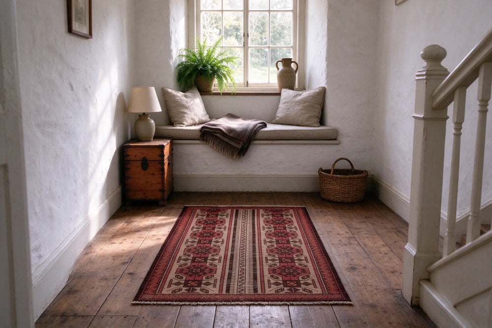 Stone cottage landing with lime-washed walls, a small red and cream Balouch rug in front of a window seat, white stair banister