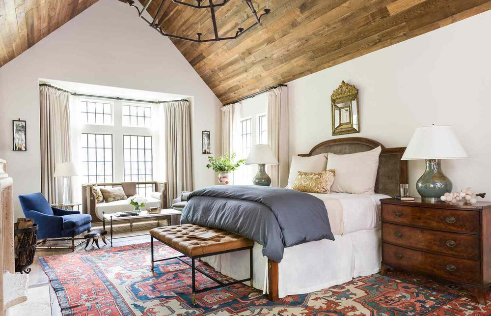 A vintage rug at the foot of a queen bed with the front legs of the bed resting on it