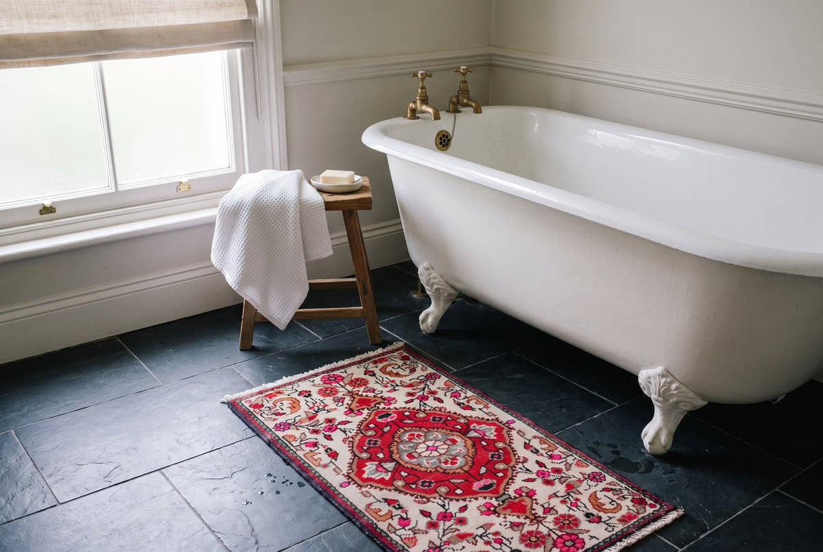 A small ivory vintage Persian Hamedan rug in a bathroom in a Victorian terraced house in Bath, England