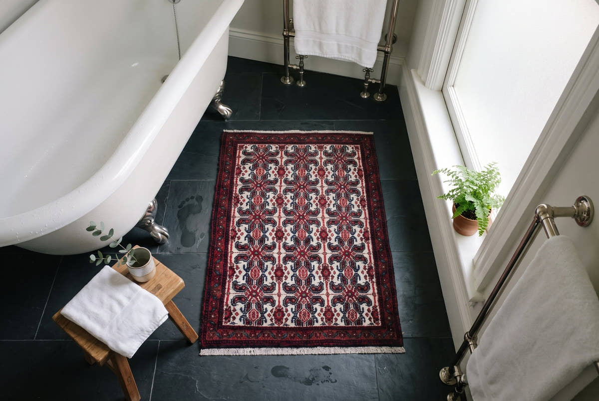 A small ivory vintage Persian Sanandaj rug beside a clawfoot tub on a slate floor in a San Francisco bathroom
